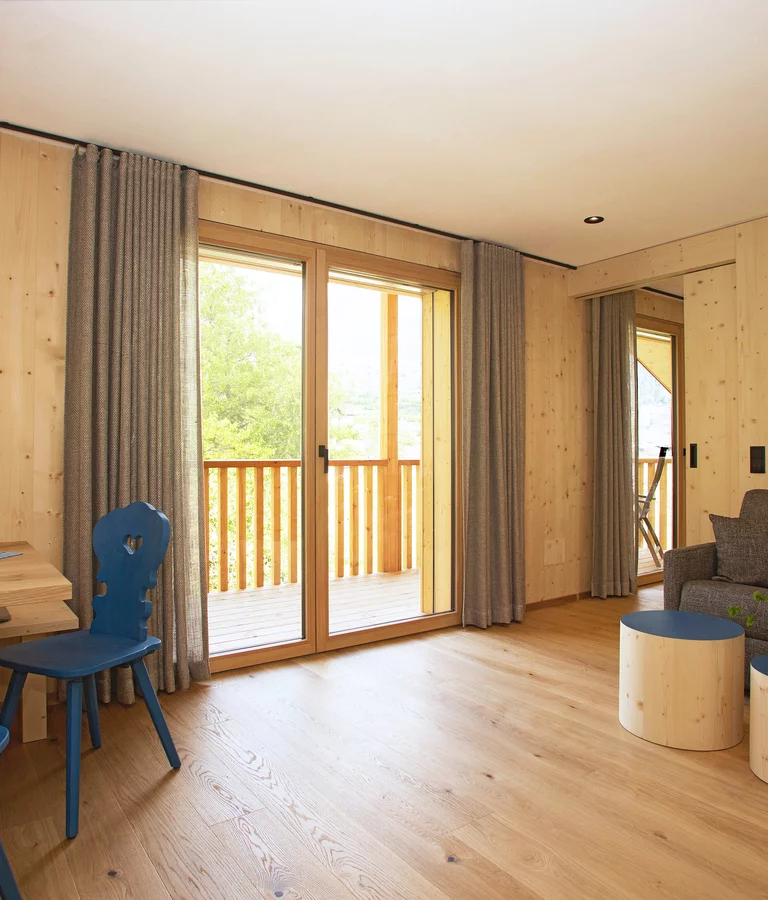 Ferienwohnung in Holz mit blauen Stühlen und Holzboden, große Balkonfenster. Ausblick Algund.