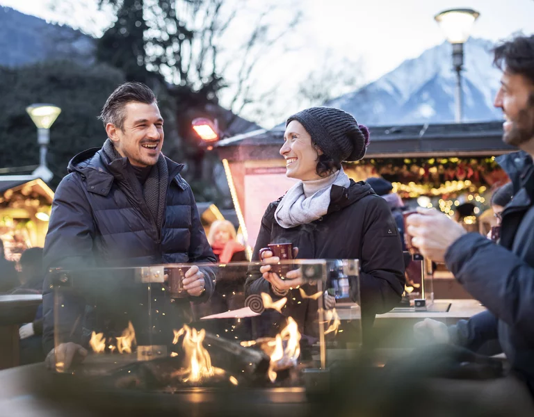 Stimmungsvolles Feuer mit drei Personen am Meraner Weihnachtsmarkt.