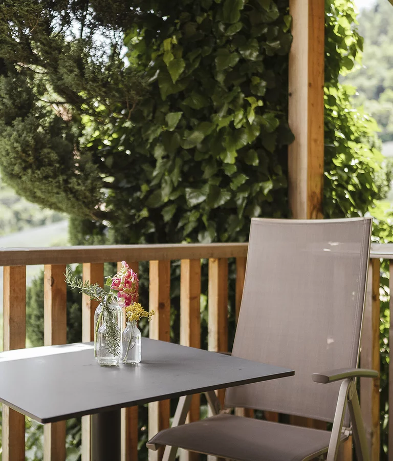 Holzbalkon mit großem Baum und einem Tisch mit zwei Liegestühlen.