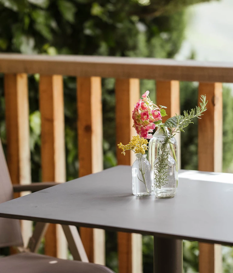 Balkon mit Holzgeländer, Tisch und Liegestuhl.