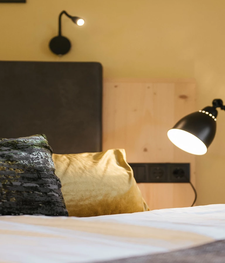 Detail Bett mit bunten Kissen und moderner Lampe.